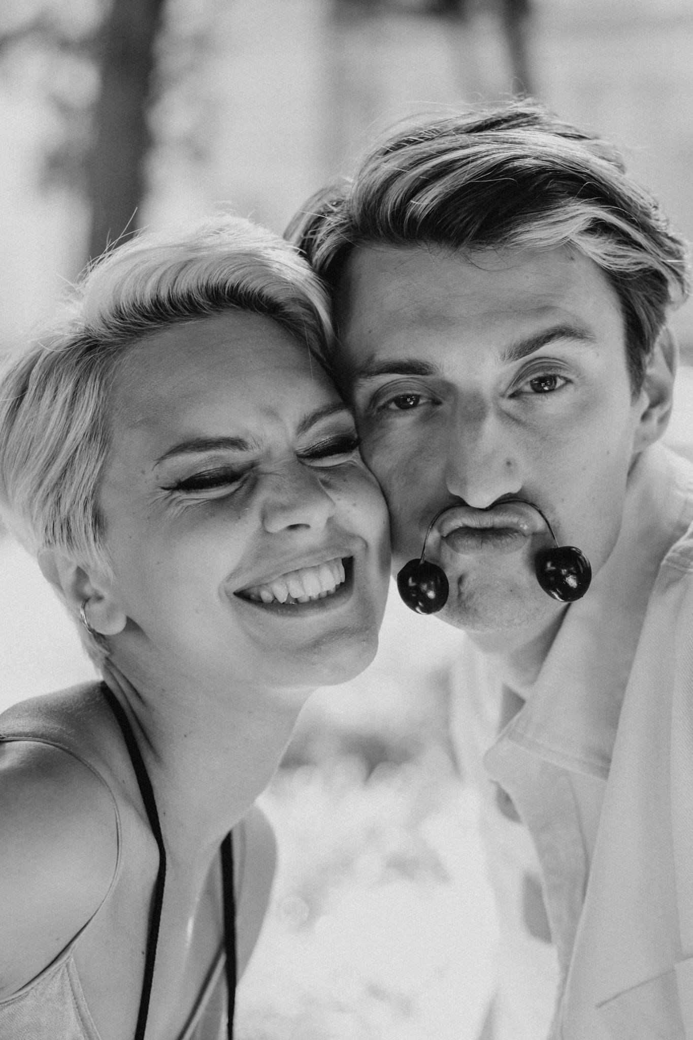 A happy couple laughing together with cherries, showcasing love and joy in a playful outdoor setting.