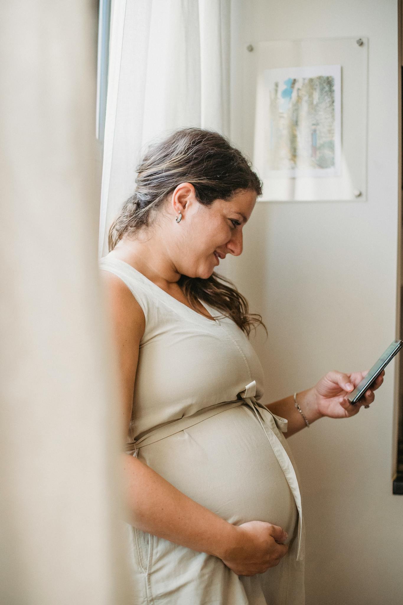 Pregnant woman joyfully using smartphone indoors, enjoying online communication.